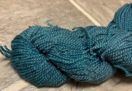 A turquoise skein of yarn that has visible dirt and damaged ends indicative of moth damage.